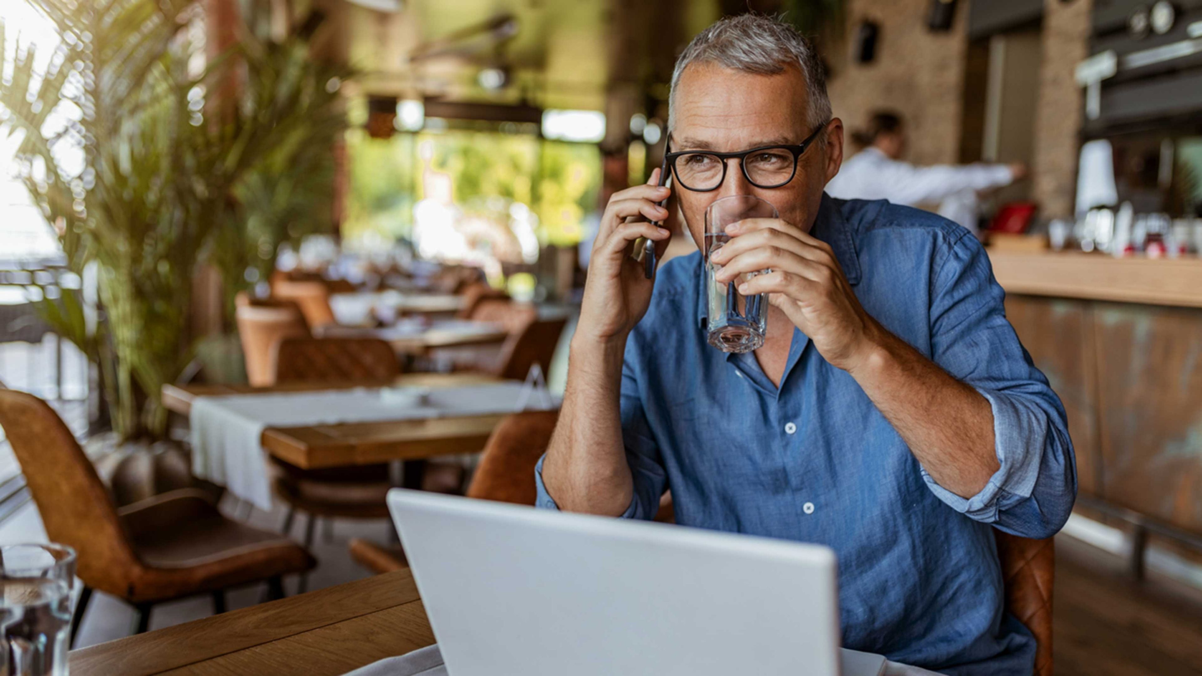 Mann sitzt im Kaffee vor dem Laptop und telefoniert mit seinem Wealth Manager und bespricht den Einfluss der AHV-Reform auf seine Pensionierungsplanung.